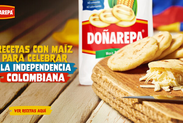 Vista de varias arepas de maíz rellenas con queso rallado sobre una tabla de madera. Al fondo, una tela de colores y contenedores con especias.
